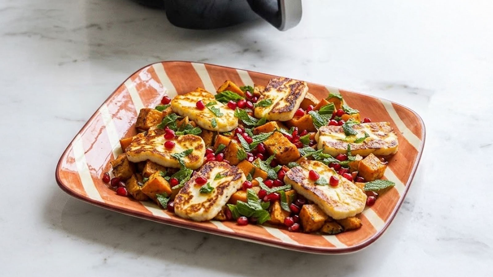 Vegetarische traybake met halloumi, zoete aardappel en granaatappel